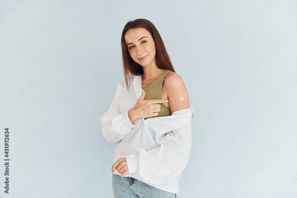 Successful vaccination. Young woman in white clothes sitting indoors against white background Successful vaccination. Young woman in white clothes sitting indoors against white background