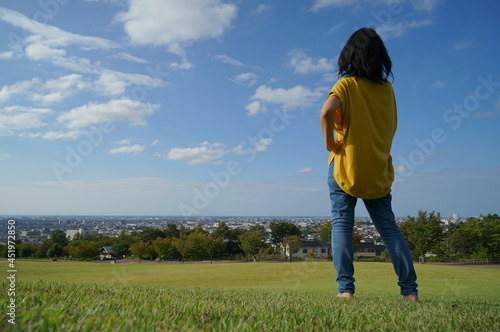 眺めの良い公園で青空のもと芝生の上で右側にいる腰に手をあてた後ろ姿の1人の女性