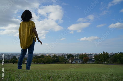 眺めの良い公園で青空のもと芝生の上で左側にいるの後ろ姿の1人の女性