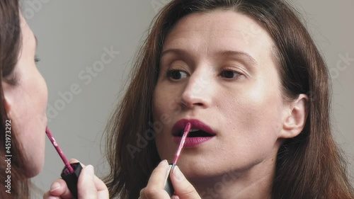 Woman standing in front of a mirror puts on makeup. paints lips with lipstick.
