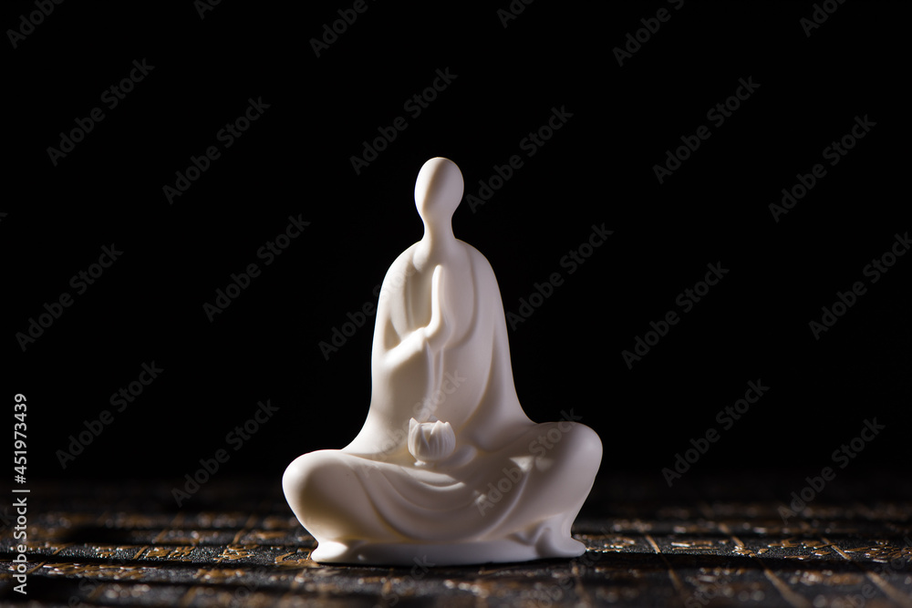 A small white Buddha figure sits with burner censer on black background A small white Buddha figure sits with burner censer on black background