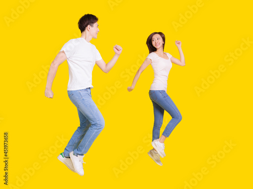 Young couple jumping up and looking each other. Isolated over yellow background.
