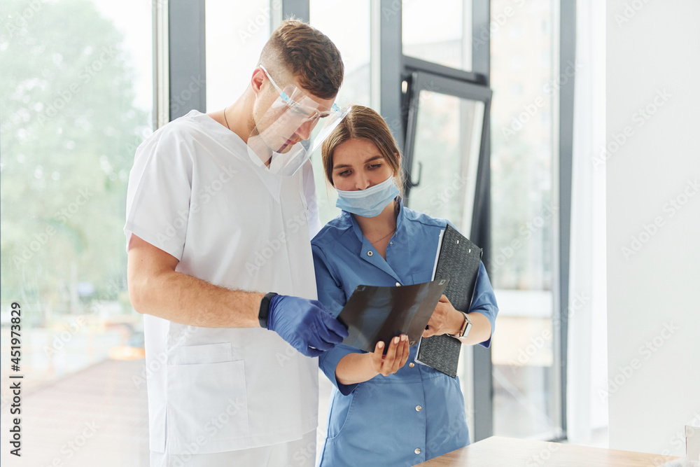 Obraz premium Looking at documents. Two doctors in uniform standing indoors and working together