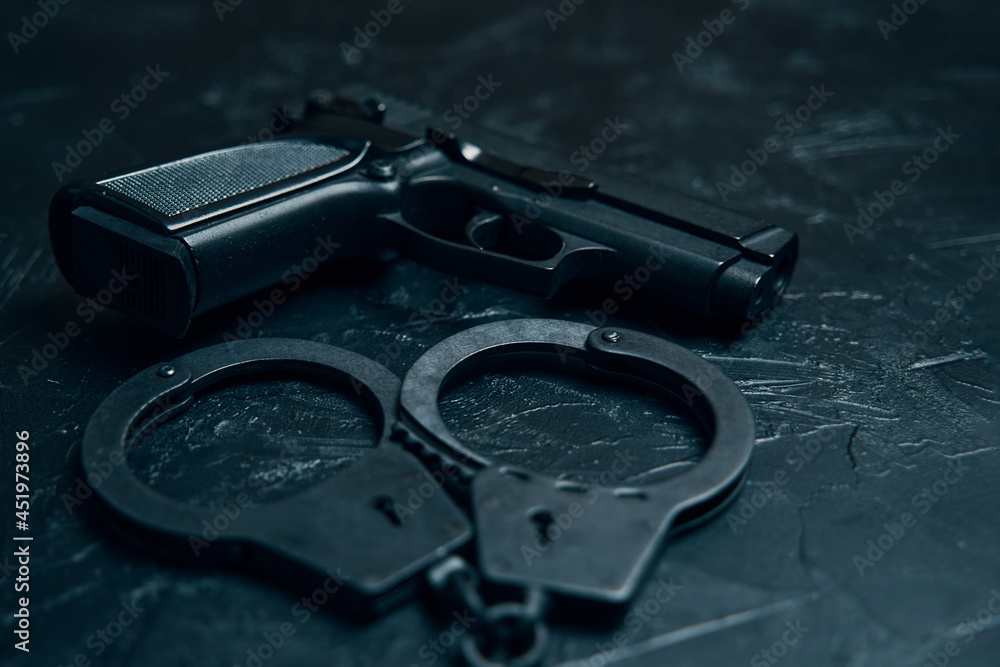 Obraz premium Pistol and handcuffs close up on black table. Ammunition for the arrest of criminals. Gun for law enforcement.