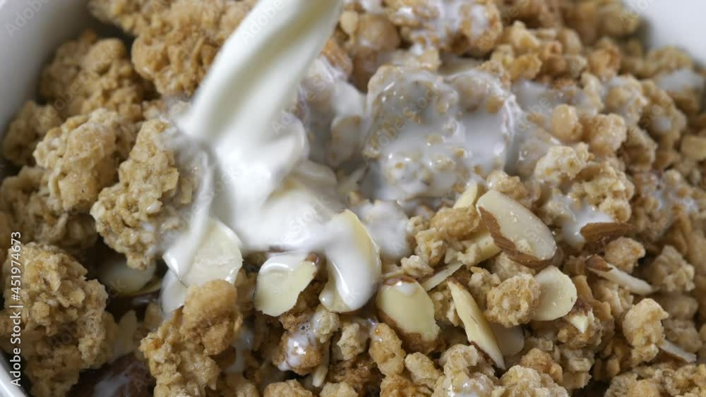 Pouring milk onto a bowl of almond granola close up super slow motion
Pouring milk onto a bowl of almond granola close up super slow motion