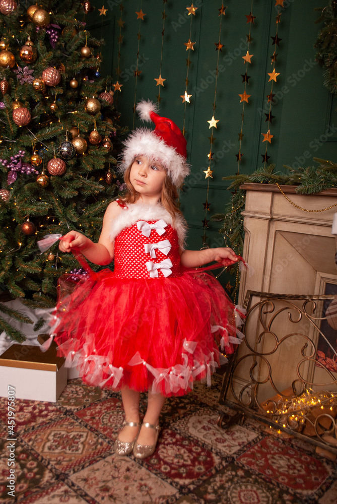 a girl in a red santa dress poses against the background of a Christmas tree in a wonderful mood. Holiday christmas and new year