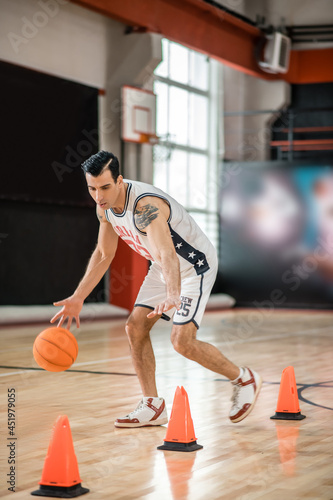 Tattoed man in white shportswear playing basket-ball and looking involved
