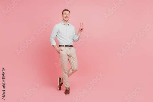 Full size photo of serious young man happy positive smile show peace cool v-sign confident isolated on pink color background