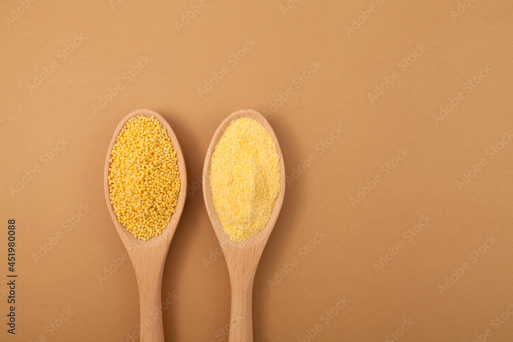 Organic Peeled Hulled millet flour and grain in wooden spoons on beige background. Top view, copy space Organic Peeled Hulled millet flour and grain in wooden spoons on beige background. Top view, copy space
