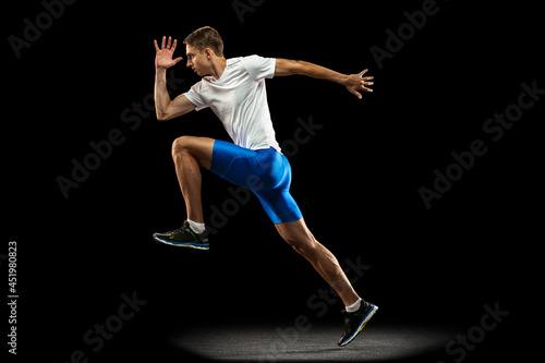 Flyer with muscular, sportive man, male athlete, runner training isolated on dark studio background with spotlight. Concept of action, motion, youth, healthy lifestyle.