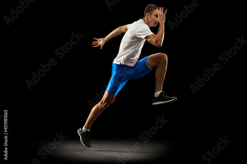 Portrait of muscular, sportive man, male athlete, runner training isolated on dark studio background with spotlight. Concept of action, motion, youth, healthy lifestyle.