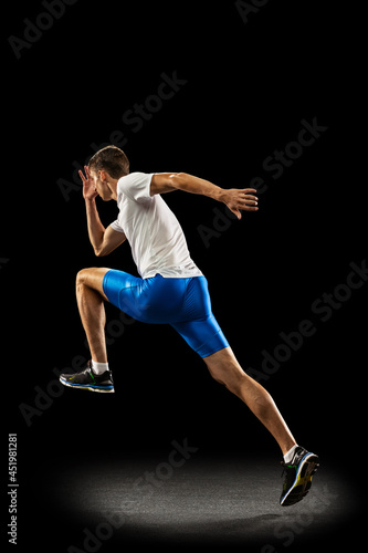 Static portrait muscular, sportive man, male athlete, runner training isolated on dark studio background with spotlight. Concept of action, motion, youth, healthy lifestyle.