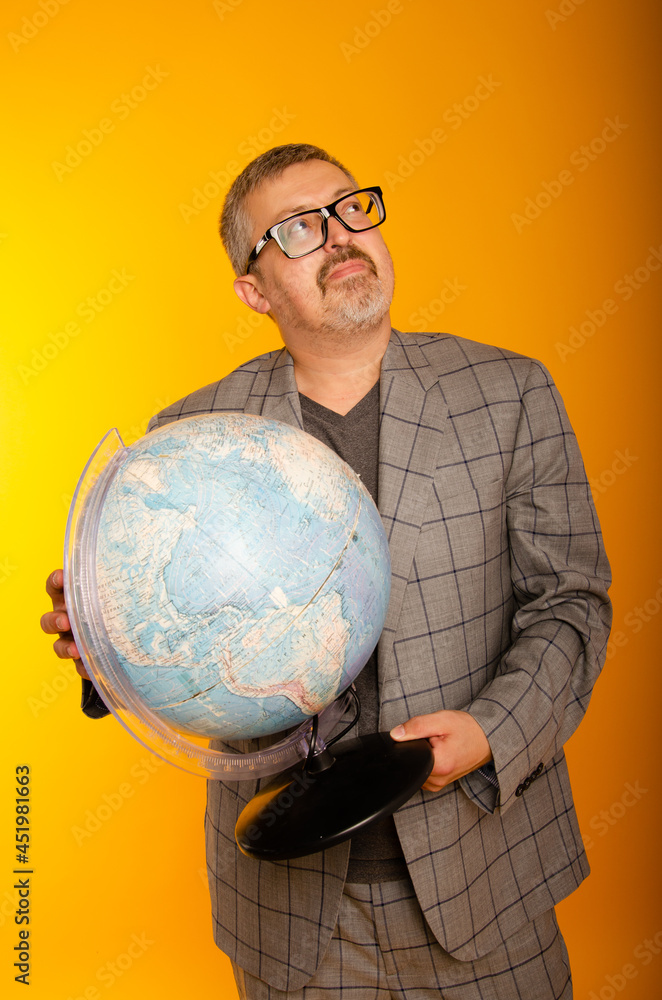An adult puzzled man with glasses on a yellow background holds a globe in his hand.
A teacher at the school teaches students geography. Knowledge day. An adult puzzled man with glasses on a yellow background holds a globe in his hand.
A teacher at the school teaches students geography. Knowledge day.