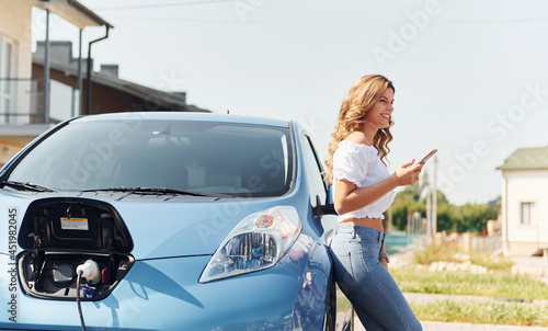 Standing near the car. Young woman in casual clothes with her electromobile outdoors at daytime © standret