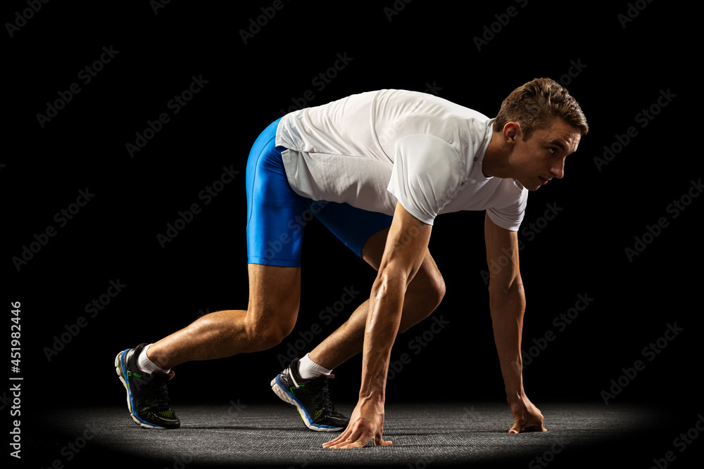 Sportive young man, male athlete, runner training isolated on dark studio background with spotlight. Concept of action, motion, youth, healthy lifestyle.