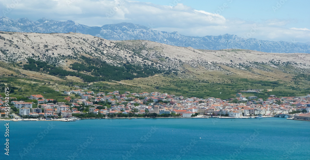 View over blue adriatic sea on village with dizzy mountains background - Island Pag, Croatia (focus on center of village)