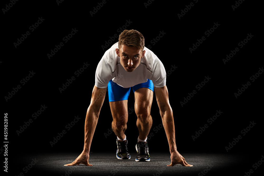 Obraz premium Sportive young man, male athlete, runner training isolated on dark studio background with spotlight. Concept of action, motion, youth, healthy lifestyle.