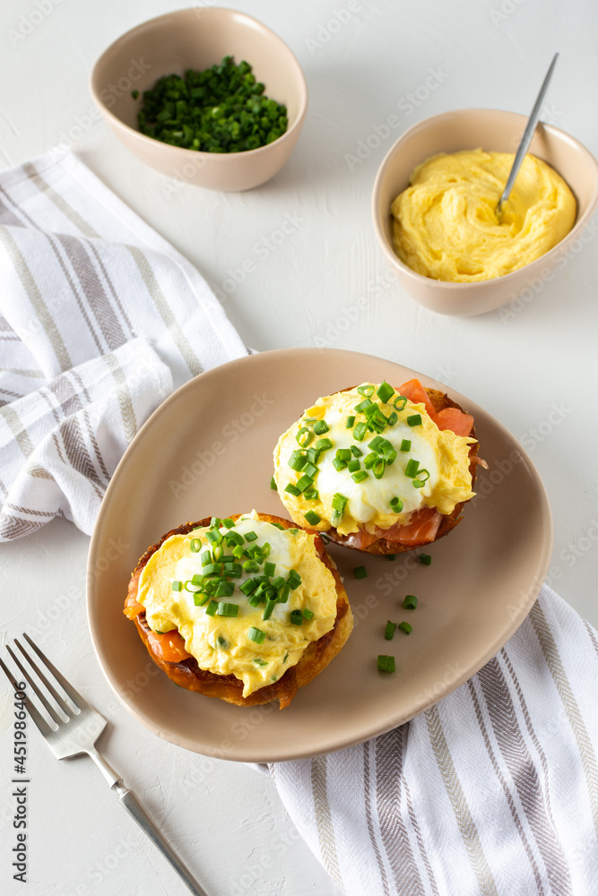 Delicious hearty breakfast, eggs Atlantic in a plate on a white background, round fried bun with salmon and eggs Benedict, hollandaise sauce and green onions