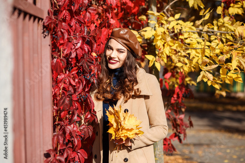 Portrait of fashionable woman next to red and yellow hedge, fall season.