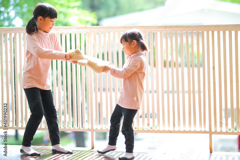 Obraz premium The little girl two asian pull the cream teddy bear at home.