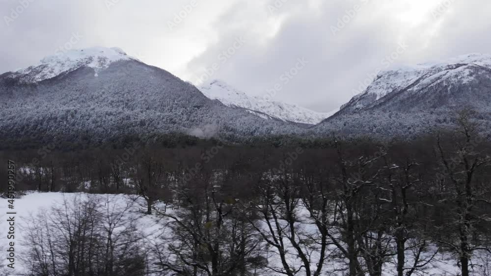 Snowy landscape with leafless trees and forests in the mountains. Cloudy. Patagonia. Drone moving to the right. Snowy landscape with leafless trees and forests in the mountains. Cloudy. Patagonia. Drone moving to the right.