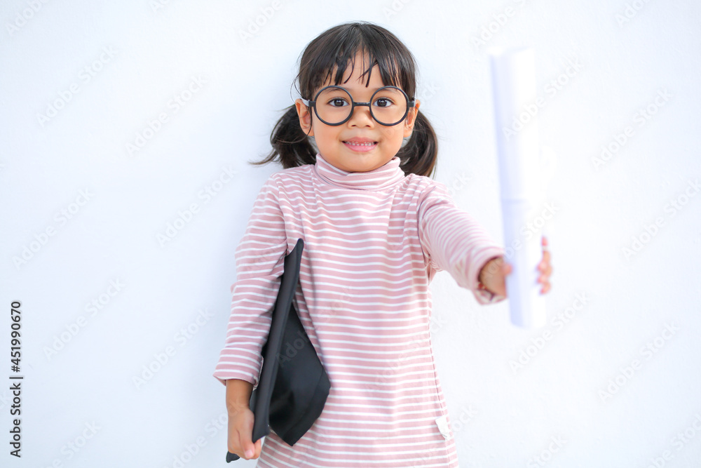 A little girl asia looks happy while celebrating his graduation and holding a diploma and graduation cap which increases the development and enhances outside the classroom learning skills concept. A little girl asia looks happy while celebrating his graduation and holding a diploma and graduation cap which increases the development and enhances outside the classroom learning skills concept.