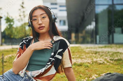 Listens to the music in headphones. Young asian woman is outdoors at daytime