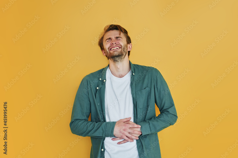 Against yellow background. Young man in casual clothes standing indoors in the studio Against yellow background. Young man in casual clothes standing indoors in the studio