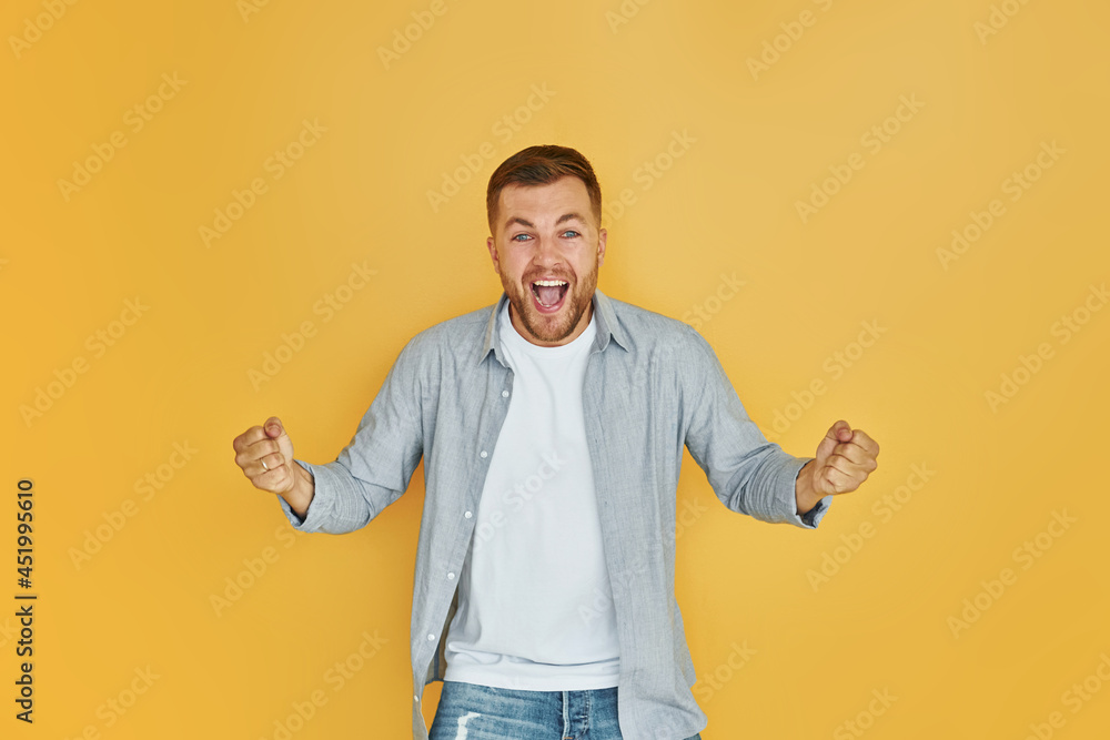 Feels good. Young man in casual clothes standing indoors in the studio Feels good. Young man in casual clothes standing indoors in the studio