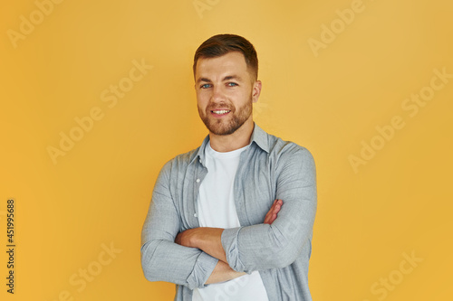 Young man in casual clothes standing indoors in the studio against orange background