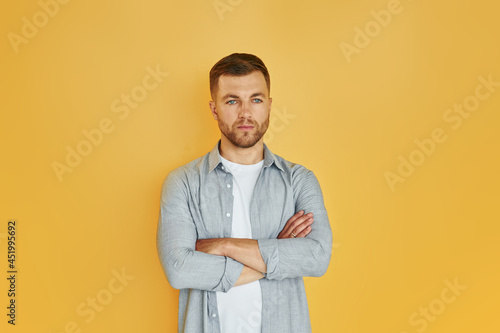 Young man in casual clothes standing indoors in the studio against orange background