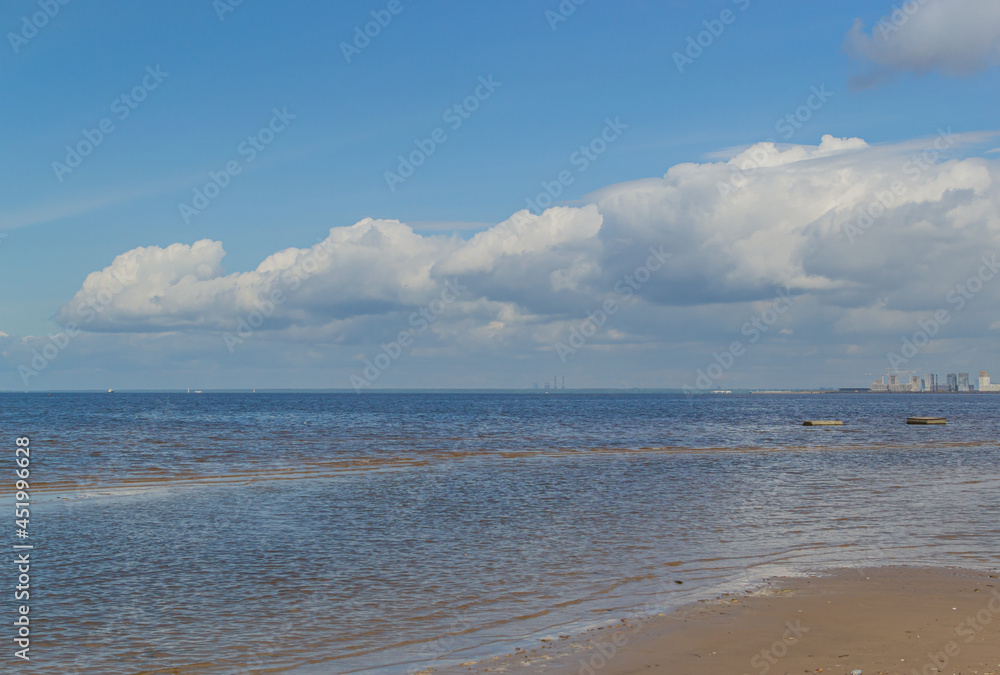 Fototapeta premium Beautiful sandy shore of the calm northern baltic sea with green stones, blue sky with big white clouds in sunny weather