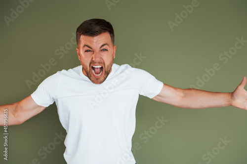 Angry young man in casual clothes standing indoors in the studio