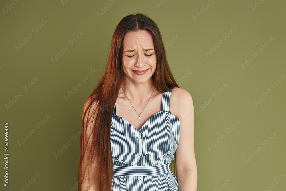 Young woman in casual clothes is crying while standing indoors in the studio Young woman in casual clothes is crying while standing indoors in the studio