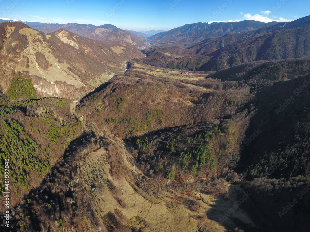 Aerial drone panorama above Malaia Valley during springtime. The river flows slowly along wooded hills and farmlands until Bradisor Lake. Massive snowed crests are guarding the valley. Malaia, Romania