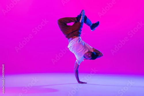 Young stylish man, hip-hop dancer dancing solo in modern clothes isolated over bright magenta background at dance hall in neon light.