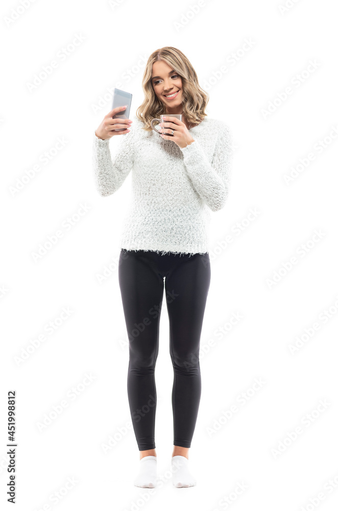 Beautiful young woman taking selfies with smart phone holding tea or coffee mug. Full body portrait isolated on white background Beautiful young woman taking selfies with smart phone holding tea or coffee mug. Full body portrait isolated on white background