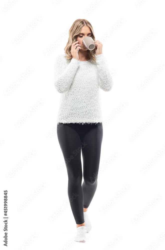 Young woman in fluffy comfy sweater drinking coffee walking and talking on the phone. Full body portrait isolated on white background Young woman in fluffy comfy sweater drinking coffee walking and talking on the phone. Full body portrait isolated on white background