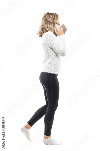 Side view of walking young woman at home drinking coffee talking on the cell phone. Full body portrait isolated on white background