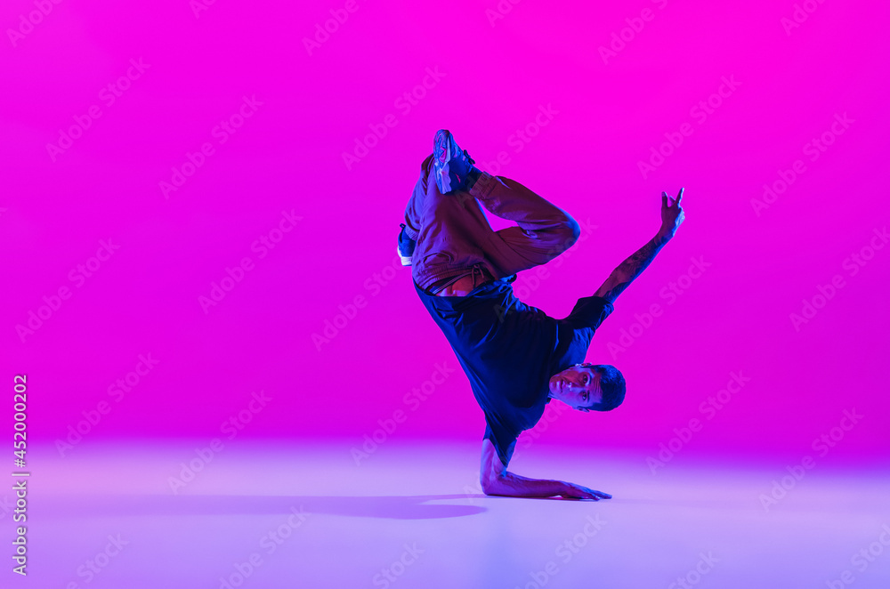 One dancing man, break dancer in action, motion in modern clothes isolated over bright magenta background at dance hall in neon light.