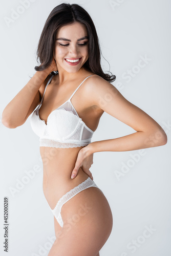 smiling young woman in lace lingerie posing with hand on hip isolated on white