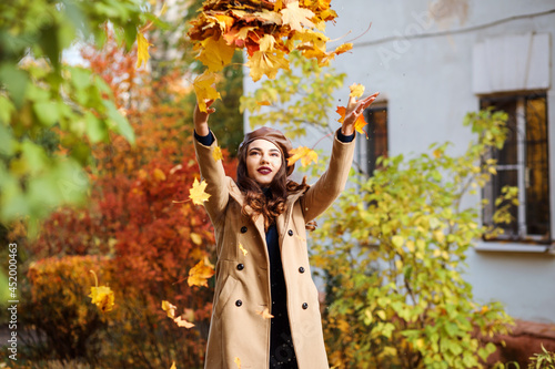 Beautiful girl throwing up yellow leaves, spending time outdoors in fall season.