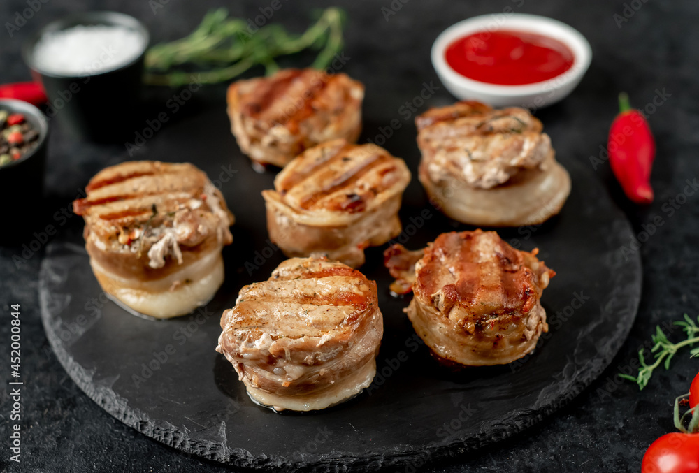 cooked grilled pork tenderloin medallions wrapped in bacon on stone background