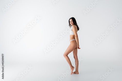 full length of young young joyful woman in lingerie posing on white