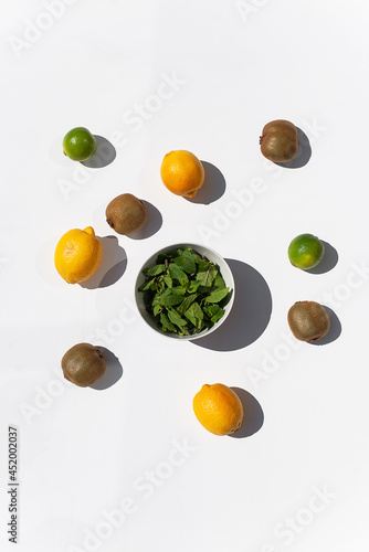 Photo of ingridients for refreshing summer lemonade cocktail with fresh citrus lime lemon and green mint and cocktail bar tools outdoors with white background flat lay style 