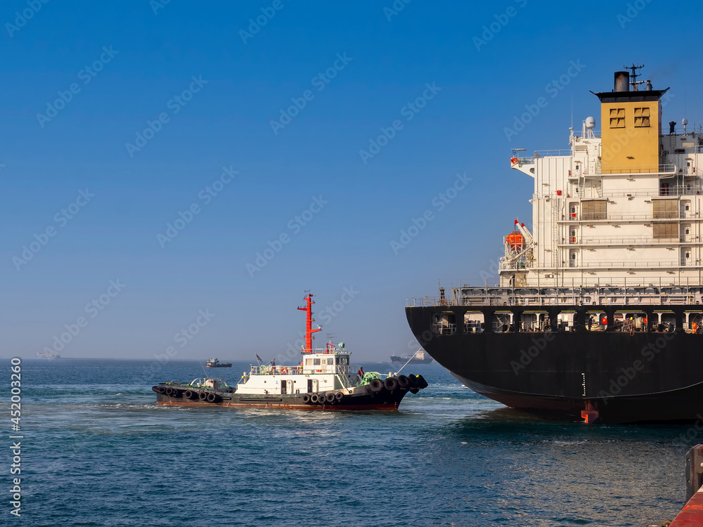 A tugboat pushing a container vessel during berthing at an industrial port. The vessel berth on arrival at port of Thailand.