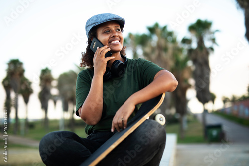 Portrait of happy african-american woman talking to the phone. Young stylish woman with skateboard outdoors..