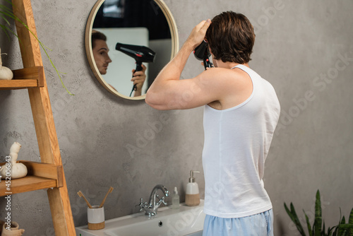 man in white tank top drying hair near mirror in bathroom