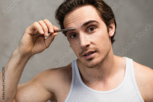 young man looking at camera while tweezing eyebrows