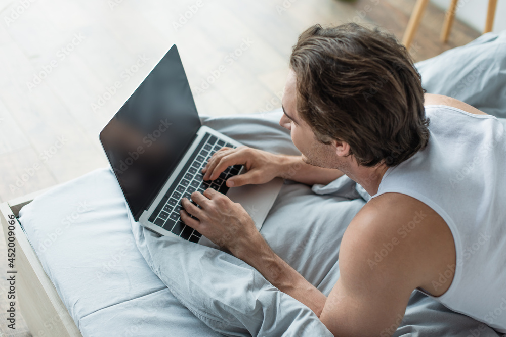 high angle view of brunette man typing on laptop with blank screen in bed high angle view of brunette man typing on laptop with blank screen in bed